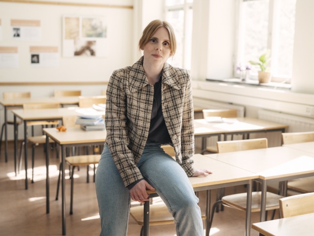 Kvinnlig gymnasielärare halvsitter på en bänk i ett klassrum Gymnasieskola - porträtt