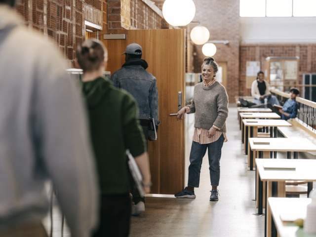 Kvinnlig gymnasielärare öppnar dörr och släpper in elever inför lektion Gymnasieskola - övrigt