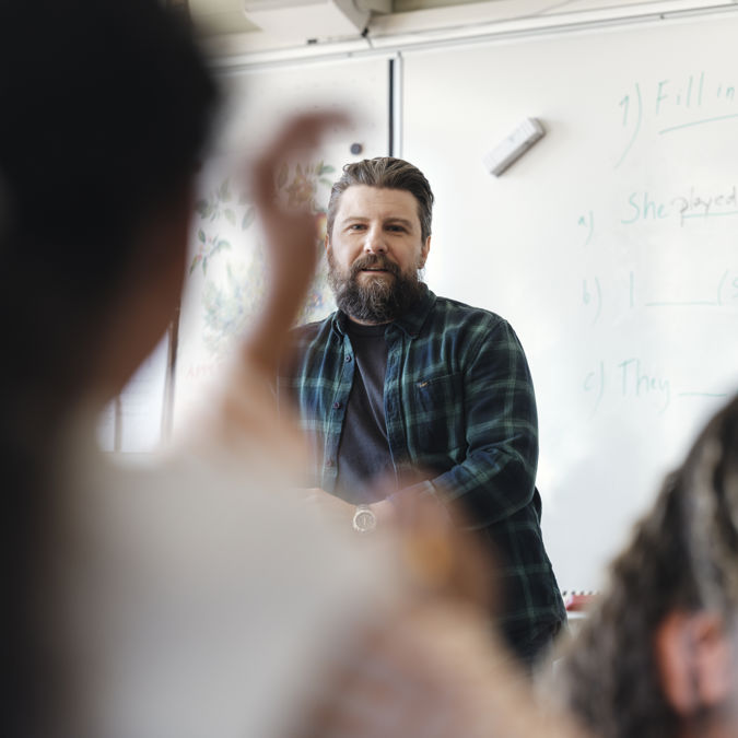 Grundskollärare med elever i klassrum - handuppräckning.