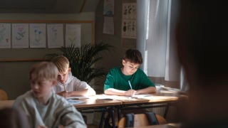 Pojkar sitter och skriver i ett klassrum.