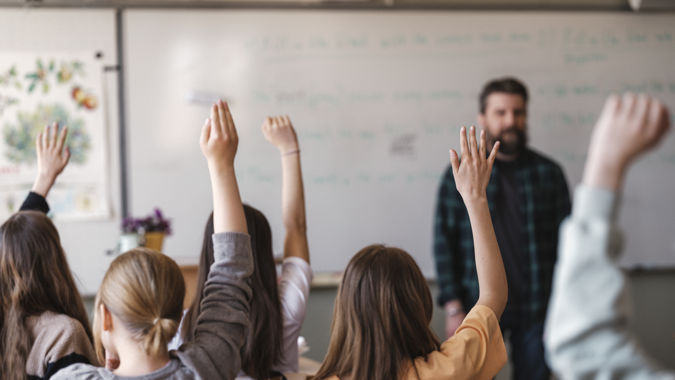 Grundskollärare med elever i klassrum - handuppräckning.