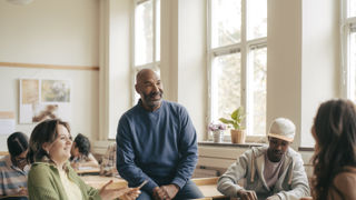 Leende gymnasielärare i samtal med elever under lektion.