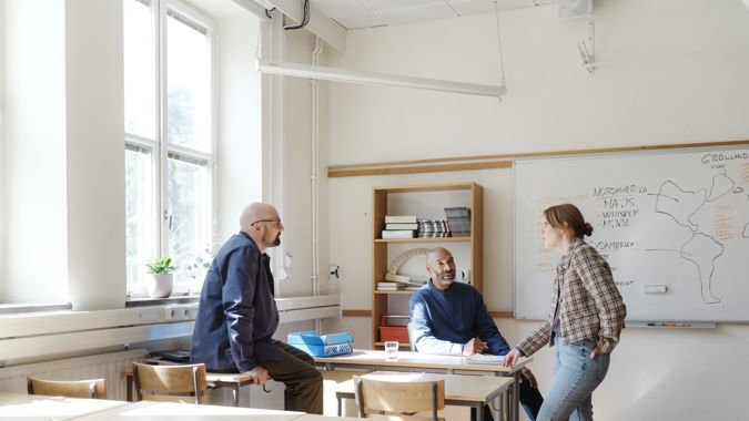 Tre gymnasielärare samtalar i ett klassrum.