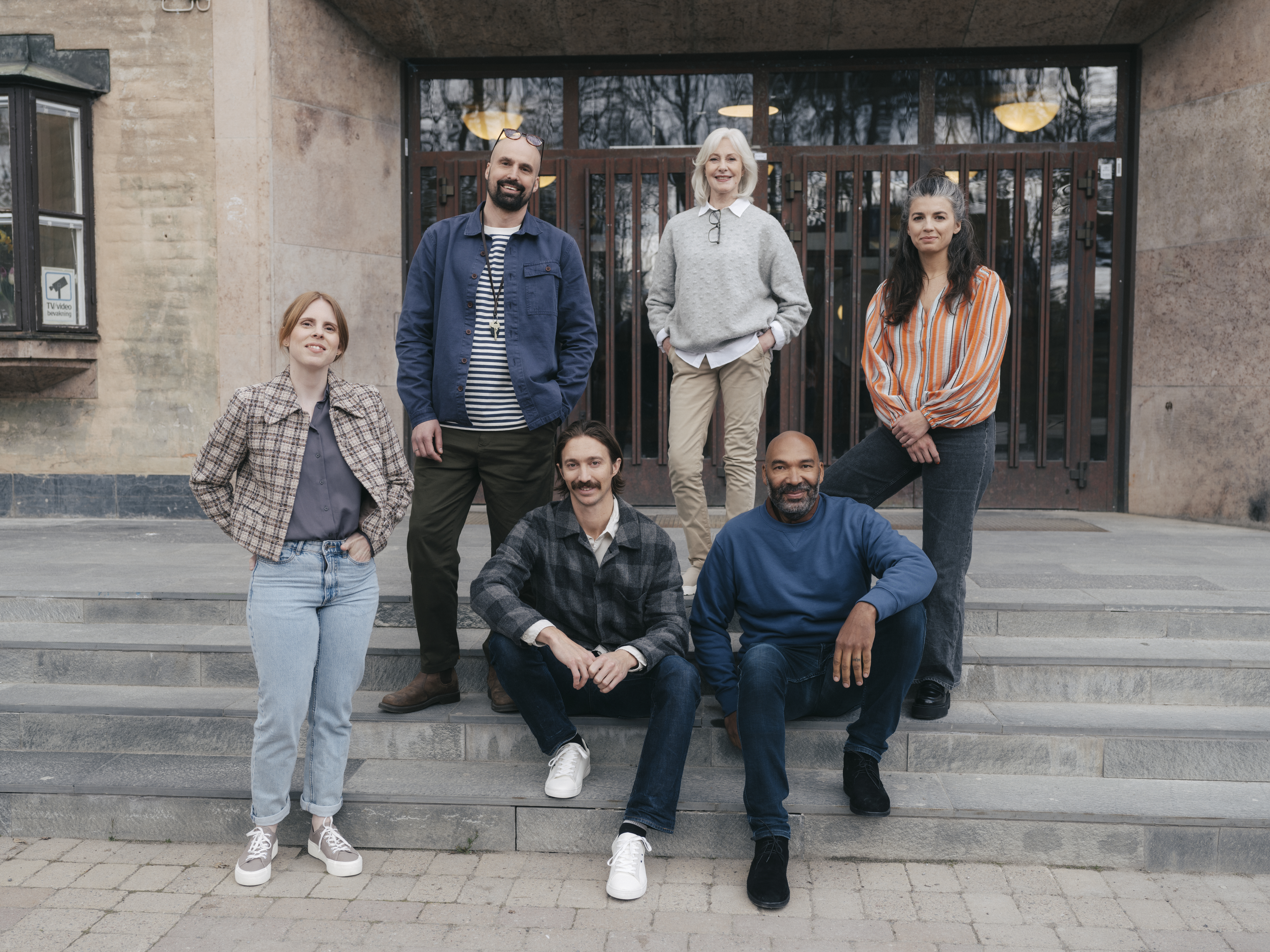 En grupp leende gymnasielärare vid trappen till ingången till en skola.