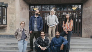 En grupp leende gymnasielärare vid trappen till ingången till en skola.