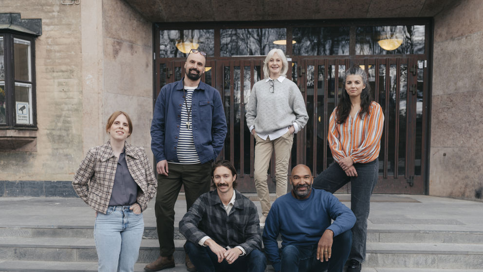 En grupp leende gymnasielärare vid trappen till ingången till en skola.