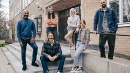 En grupp leende gymnasielärare vid trappen till ingången till en skola.