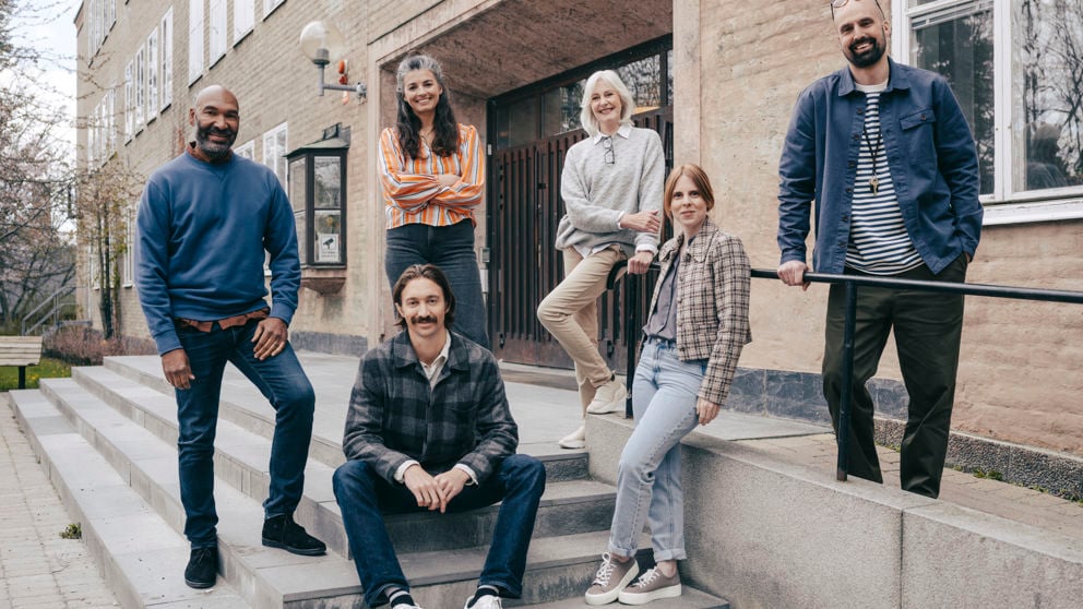 En grupp leende gymnasielärare vid trappen till ingången till en skola.