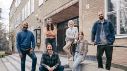 En grupp leende gymnasielärare vid trappen till ingången till en skola.