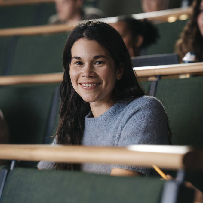 Leende kvinnlig student under föreläsning i aula vid högskola.