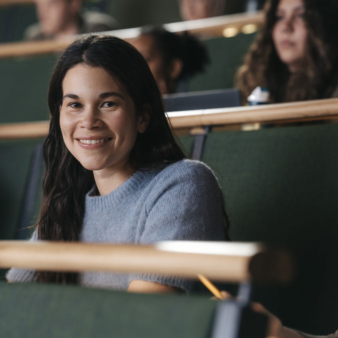 Leende kvinnlig student under föreläsning i aula vid högskola.