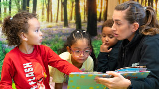 Förskollärare med elever tittar i bok på Skogsbackaskolans förskola i Botkyrka.