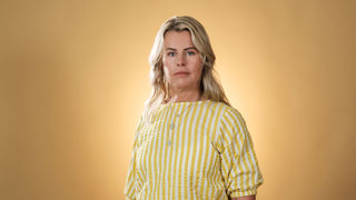 Allvarlig Anna Olskog, iklädd gulrandig dress framför gul bakgrund.