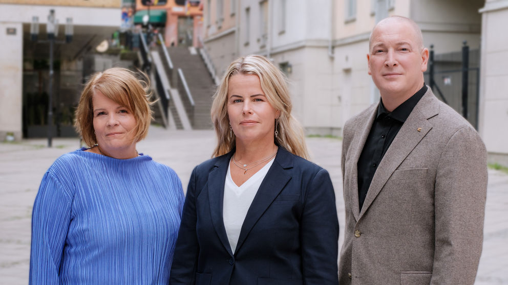 Presidiet stående utomhus med neutrala miner. Pia Rizell i blå dress, Anna Olskog i vit tröja och mörk kavaj och Robin i svart tröja och grå kostym.