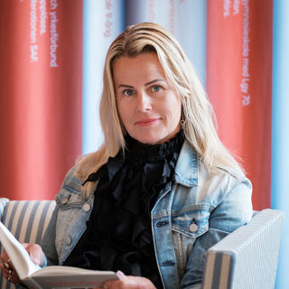 Sveriges Lärares ordförande Anna Olskog i svart tröja och blå jeansjacka läser en bok.