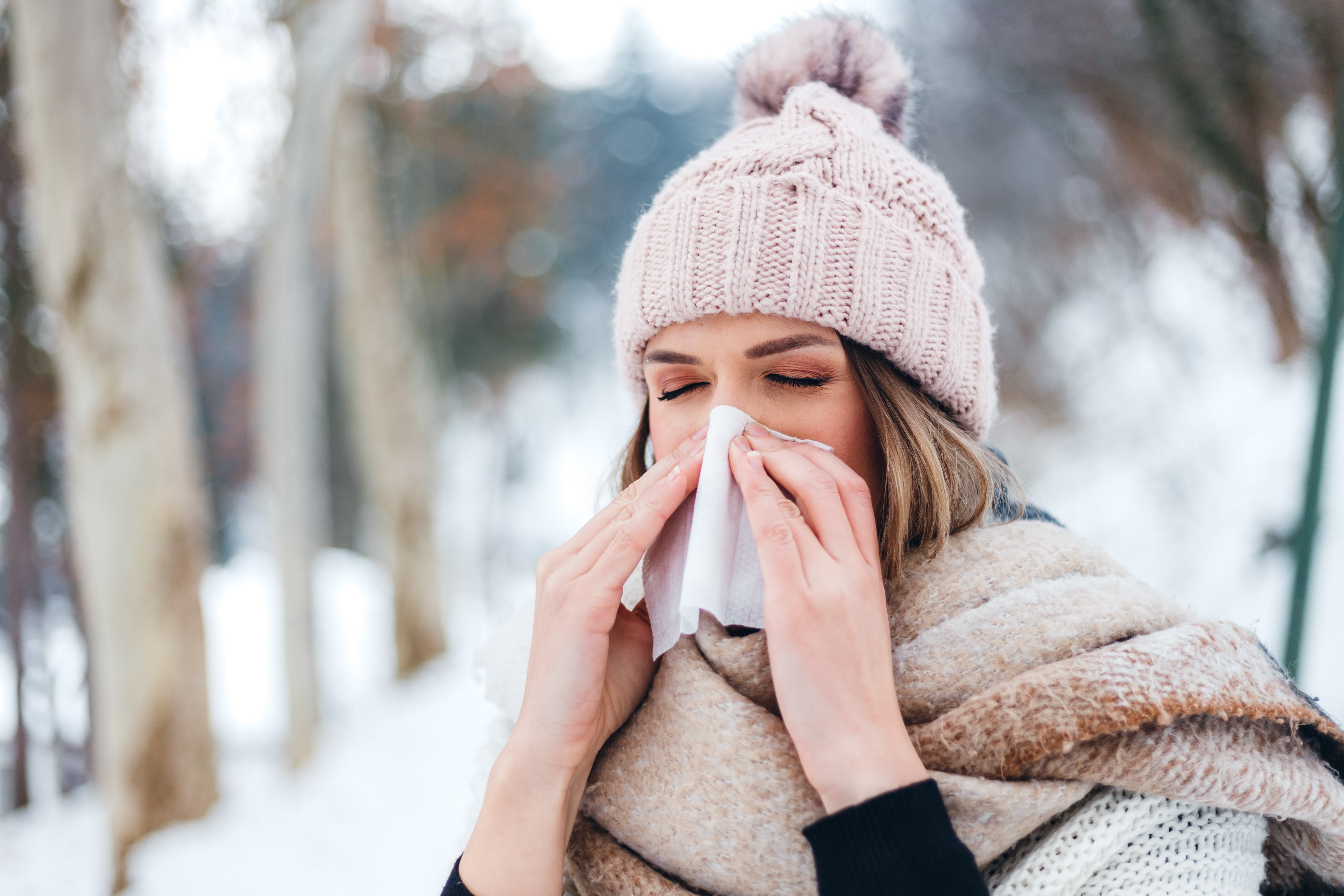 Portrait of a young beautiful woman using facial tissue in the snow.