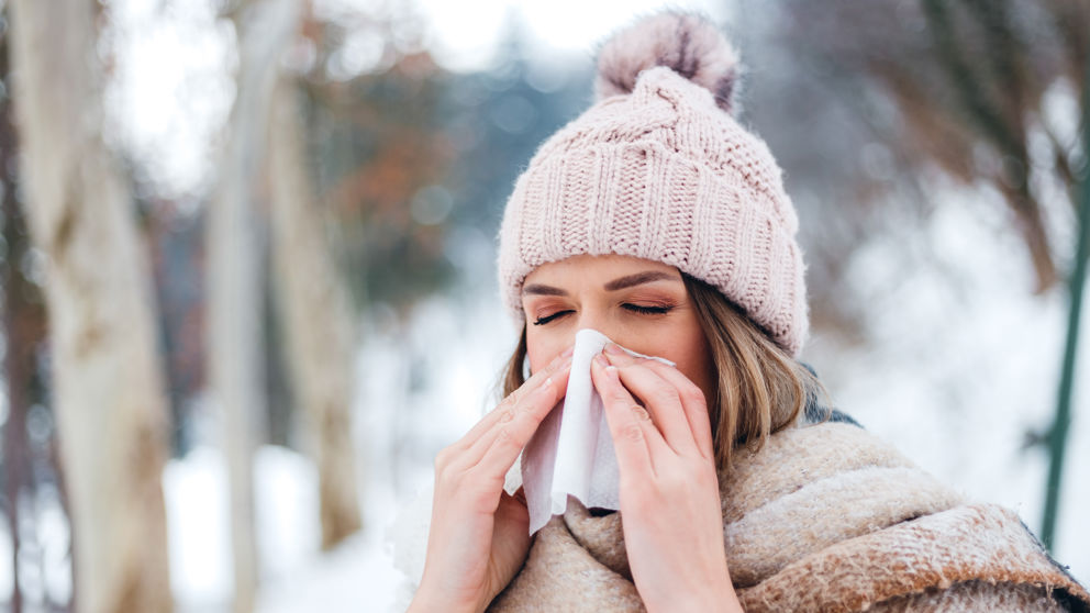 Portrait of a young beautiful woman using facial tissue in the snow.