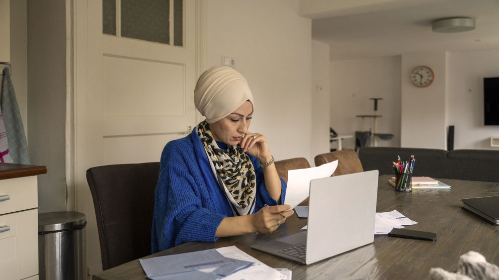 Adult woman wearing a hijab working on a laptop at a home office, thoughtfully holding a pen and analyzing documents. Adult woman wearing a hijab working on a laptop at a home office, thoughtfully holding a pen and analyzing documents. Adult woman wearing a hijab working on a laptop at a home office, thoughtfully holding a pen and analyzing documents.