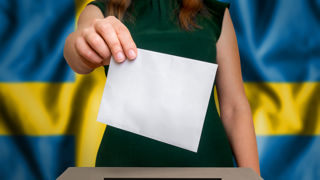 Election in Sweden - voting at the ballot box. The hand of woman putting her vote in the ballot box. Flag of Sweden on background.