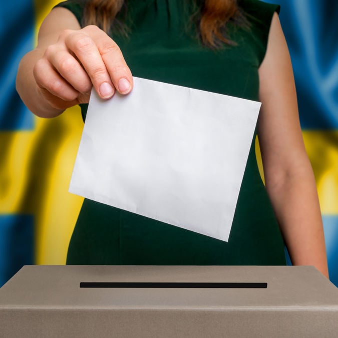 Election in Sweden - voting at the ballot box. The hand of woman putting her vote in the ballot box. Flag of Sweden on background.