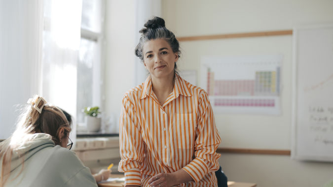 Leende gymnasielärare med elever under lektion.