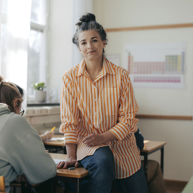 Leende gymnasielärare med elever under lektion.